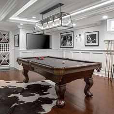 a pool table in the middle of a living room with pictures on the wall behind it