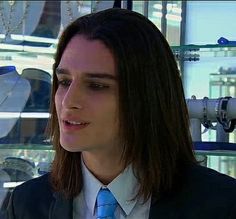 a young man wearing a suit and tie in front of glass shelves with dishes on them