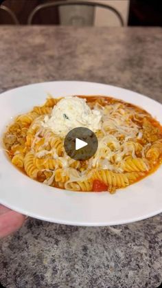 a white plate topped with pasta and cheese on top of a marble counter next to a person's hand