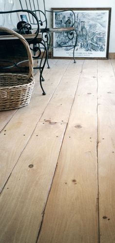 a wooden floor in a living room with pictures on the wall and a wicker basket next to it