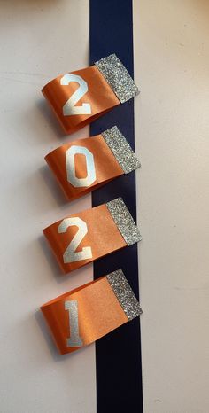 three orange and silver ribbons with numbers on them hanging from a white wall next to a clock