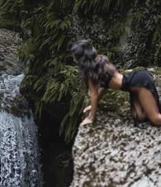 a woman sitting on top of a rock next to a waterfall