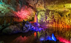 the inside of a cave with colorful lights on it's walls and water in the foreground