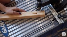 a person working on a piece of wood with a machine in the back ground behind them