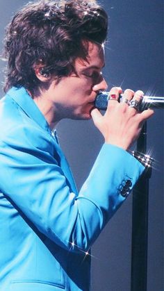 a male in a blue suit is holding a microphone to his mouth and singing into it