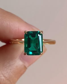 a woman's hand holding an emerald ring with the stone on top of it