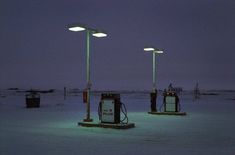 three gas pumps sitting in the middle of a snow covered field with lights on them