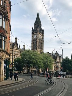 a man riding a bike down a street next to tall buildings and a clock tower