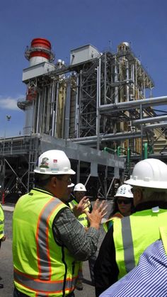 some people wearing hard hats and vests talking to each other in front of an oil refinery