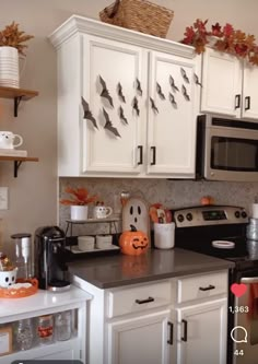 a kitchen decorated for halloween with white cabinets and black counter tops, pumpkins on the shelves