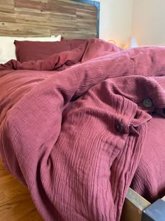 an unmade bed with red linens on top of it and wooden headboard