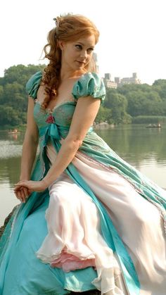 a woman in a blue and white dress is sitting on a rock by the water