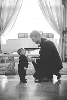 a man kneeling down next to a little boy who is holding his hand out for him