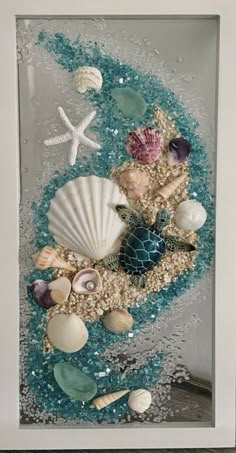 an ocean scene with shells, starfish and other things in the sand under a shadow box