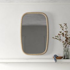 a mirror sitting on top of a mantle next to a vase