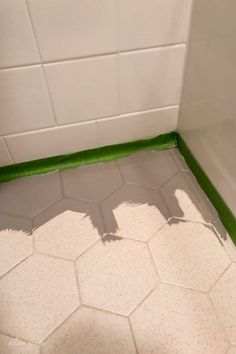 a bathroom with white tile and green trim on the shower wall, next to a tiled floor