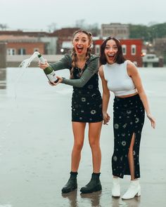 two young women are laughing and holding wine bottles in their hands while standing on the wet ground