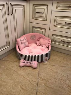 a pink dog bed in the middle of a kitchen with white cupboards and drawers