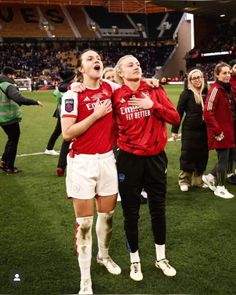 two female soccer players standing next to each other in front of a crowd on a field