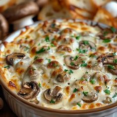 a casserole dish with mushrooms and cheese in it on a table next to bread