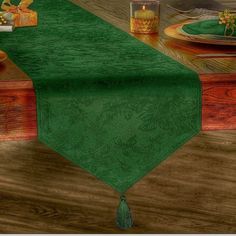 a green table runner on top of a wooden table next to a cup and candle