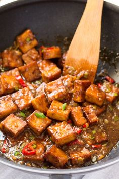 tofu being cooked in a pan with a wooden spoon