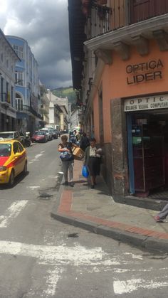 people are walking on the sidewalk in front of an orange and white building with a yellow car parked next to it