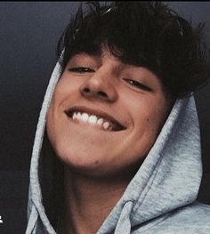 a smiling young man wearing a gray hoodie with his eyes closed and head tilted to the side