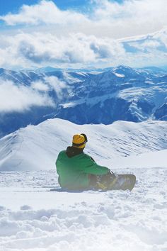 a snowboarder sitting in the snow on top of a mountain