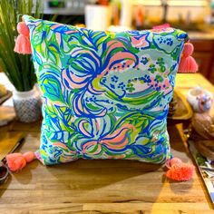 a colorful pillow sitting on top of a wooden table next to a potted plant