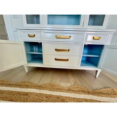 a white cabinet with blue glass doors and gold handles on the bottom, next to a rug