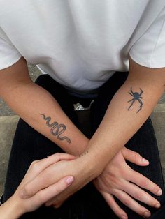 two people sitting on the ground with their arms crossed and one person has tattoos on his arm