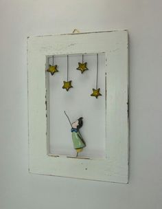 a white frame with stars hanging from it's sides and a small doll in the middle