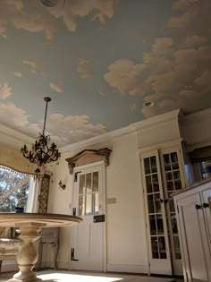 a dining room with a chandelier and clouds painted on the ceiling