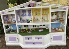 a doll house with furniture and accessories on display in front of some trees, grass and bushes