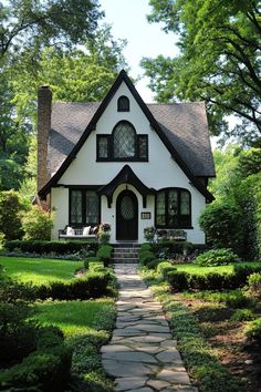 White Tudor house with charming black trim, nestled in a lush garden. The charming fusion of history and contemporary flair in modern Tudor houses can transform your living space from “just nice” to “royalty-approved.” White Tudor House, Tudor Cottage House Plans, White House With Black Trim, House With Black Trim, Building Reference, Tudor Cottage