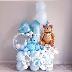 a teddy bear sitting on top of a table surrounded by balloons and other items for a baby's first birthday