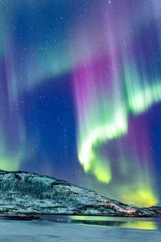 the northern lights shine brightly in the sky above snow covered mountains and lake with water below