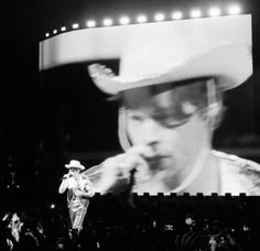 a black and white photo of a man in a cowboy hat on stage with his hand to his mouth