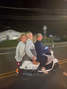 two women riding on the back of a white scooter down a street at night