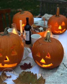 three carved pumpkins sitting on top of a table next to wine bottles and leaves