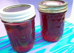 two jars filled with red liquid sitting on top of a blue and white table cloth