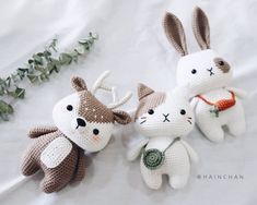 three crocheted stuffed animals sitting next to each other on a white sheet with greenery in the background