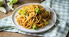 a white plate topped with pasta and broccoli on top of a wooden table