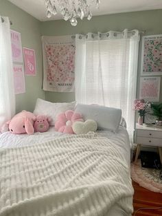 a white bed topped with two pink stuffed animals next to a window covered in curtains