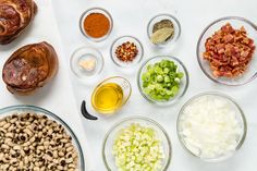 an assortment of ingredients are shown in bowls on a white table top, including beans, onions, and other foodstuffs