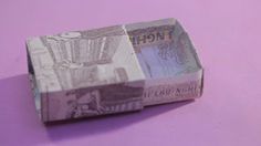 an origami money box sitting on top of a pink surface with purple background