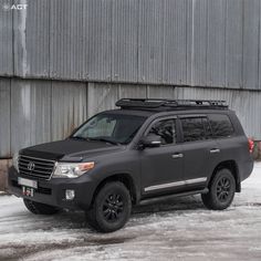 a gray suv parked in front of a building with snow on the ground next to it