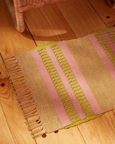 a pink and green rug sitting on top of a wooden floor next to a chair