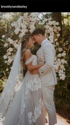 a bride and groom standing in front of a flower covered arch with white flowers on it